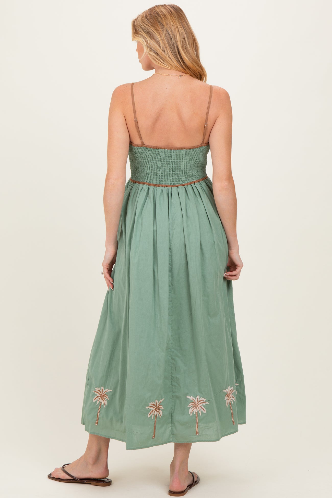 woman wearing a green maternity maxi dress with a smocked bodice and palm tree embroidery at the hem