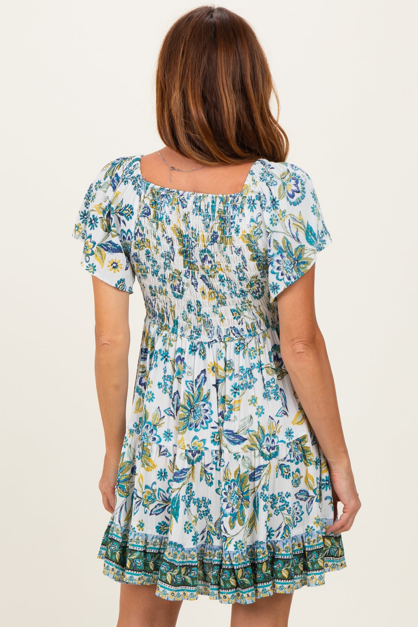 woman wearing a white floral print smocked mini dress with short sleeves and a ruffled hem