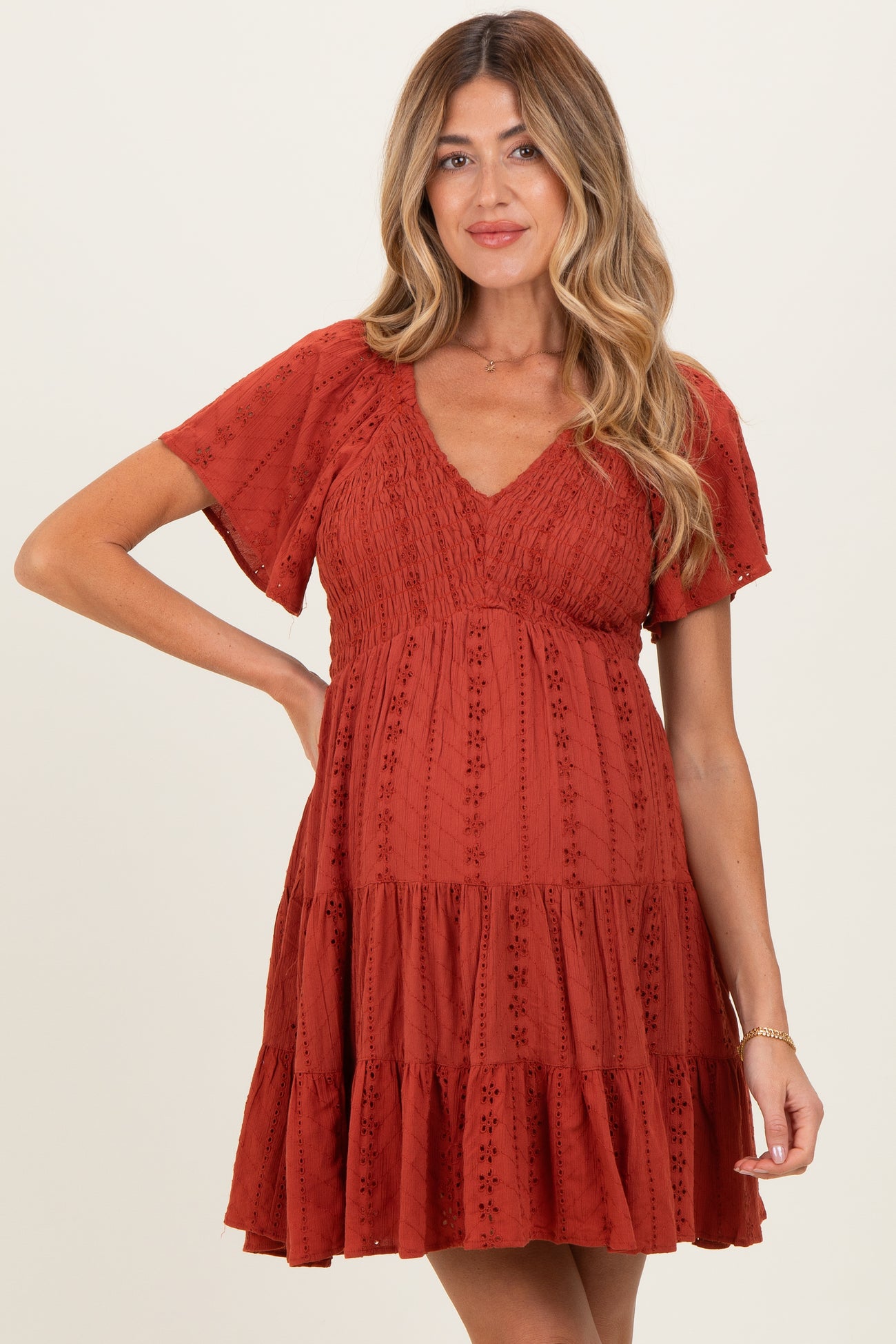 woman wearing a rust colored maternity dress with short sleeves and a tiered skirt, showing her baby bump