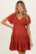 woman wearing a rust colored maternity dress with short sleeves and a tiered skirt, showing her baby bump