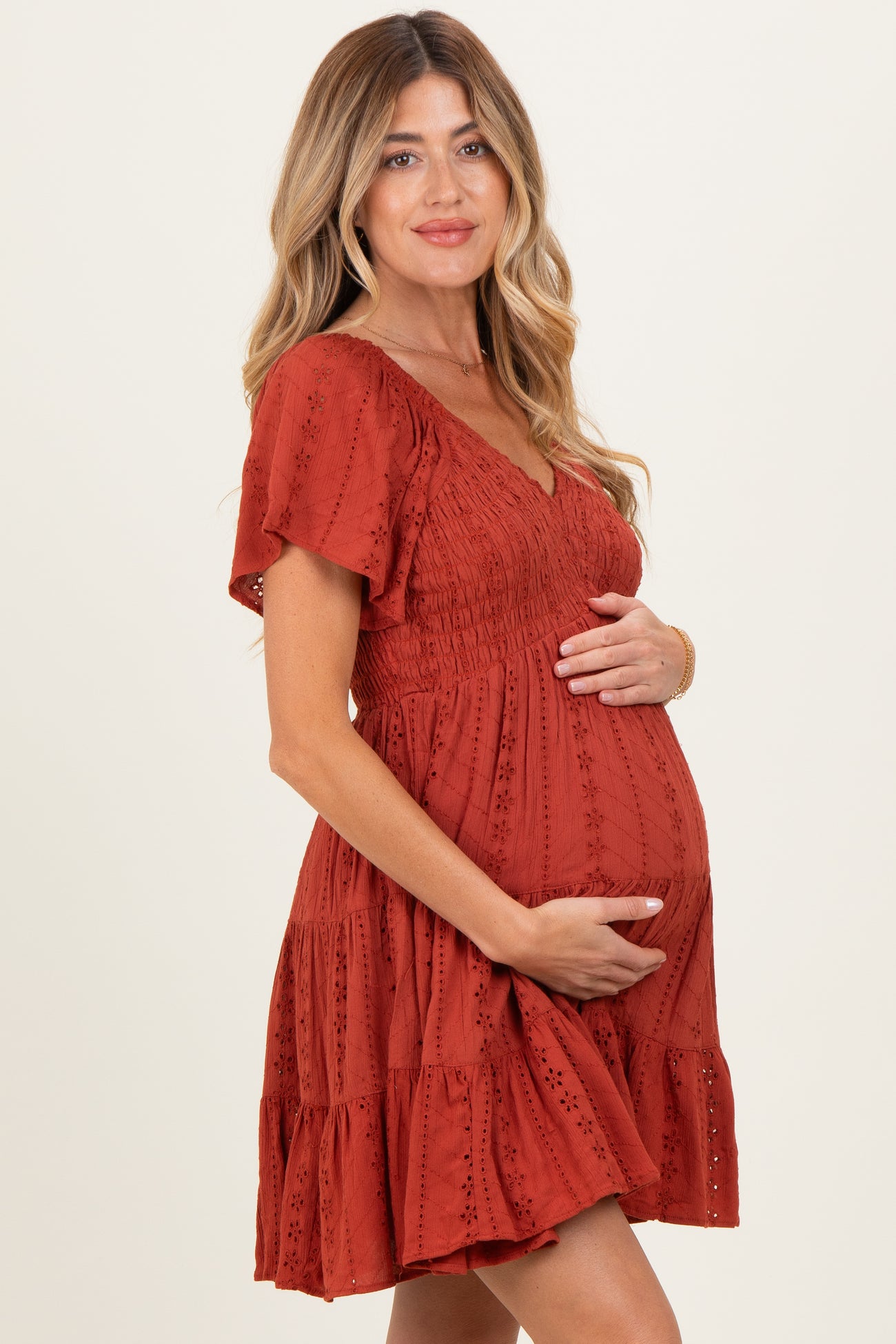 woman wearing a rust-colored maternity dress with a v-neck and flutter sleeves, cradling her baby bump