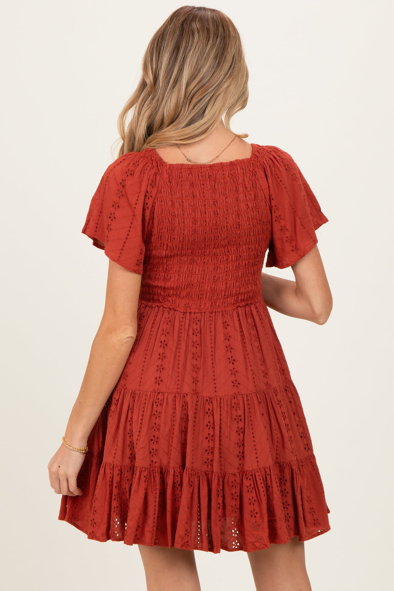 woman wearing a rust red short sleeve maternity dress with a smocked bodice and tiered skirt from the back
