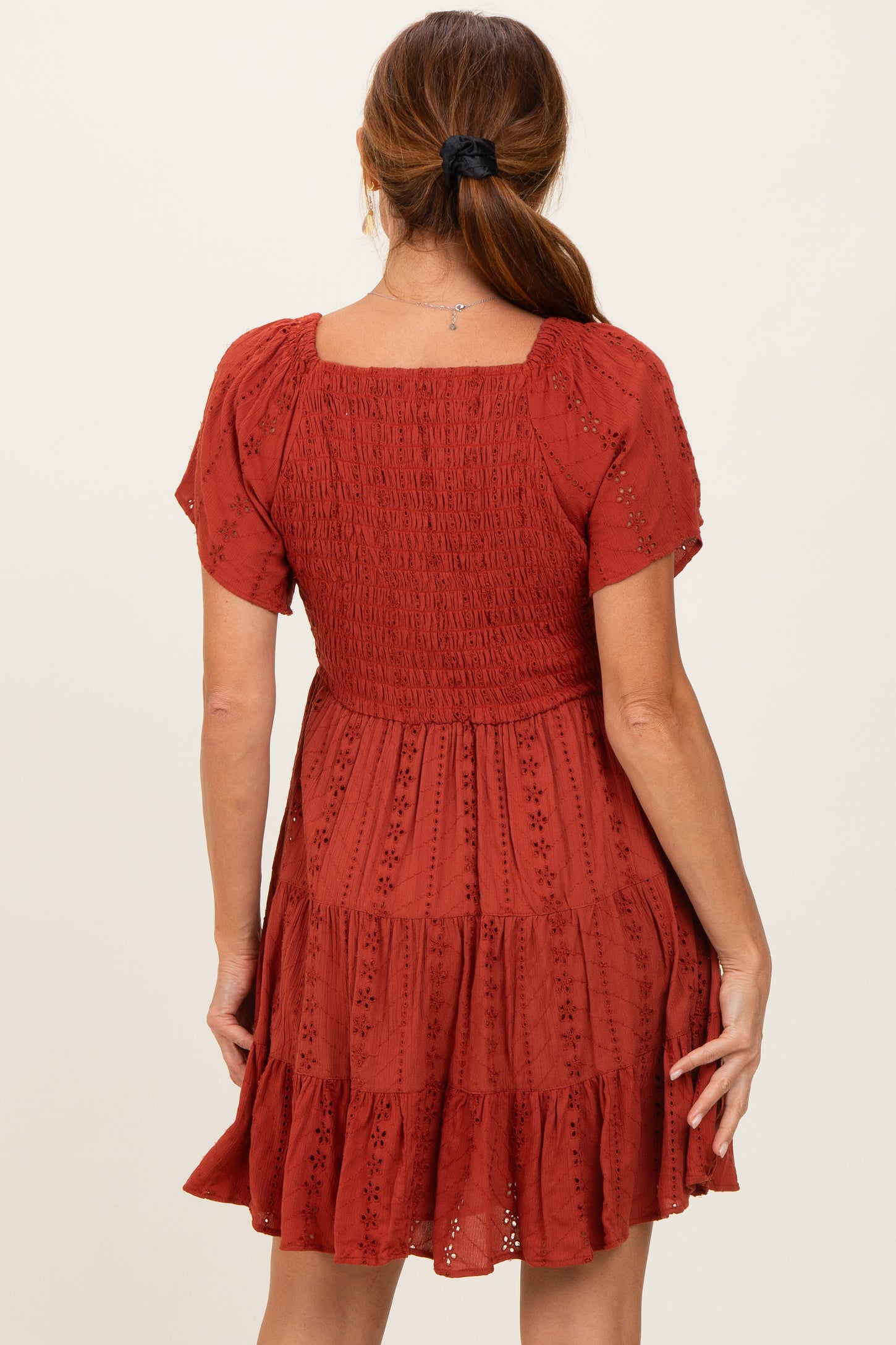 woman wearing a rust-colored short sleeve dress with a smocked bodice and tiered skirt, shown from the back