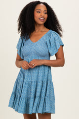 woman wearing a blue floral short sleeve dress with a tiered skirt and a v-neckline