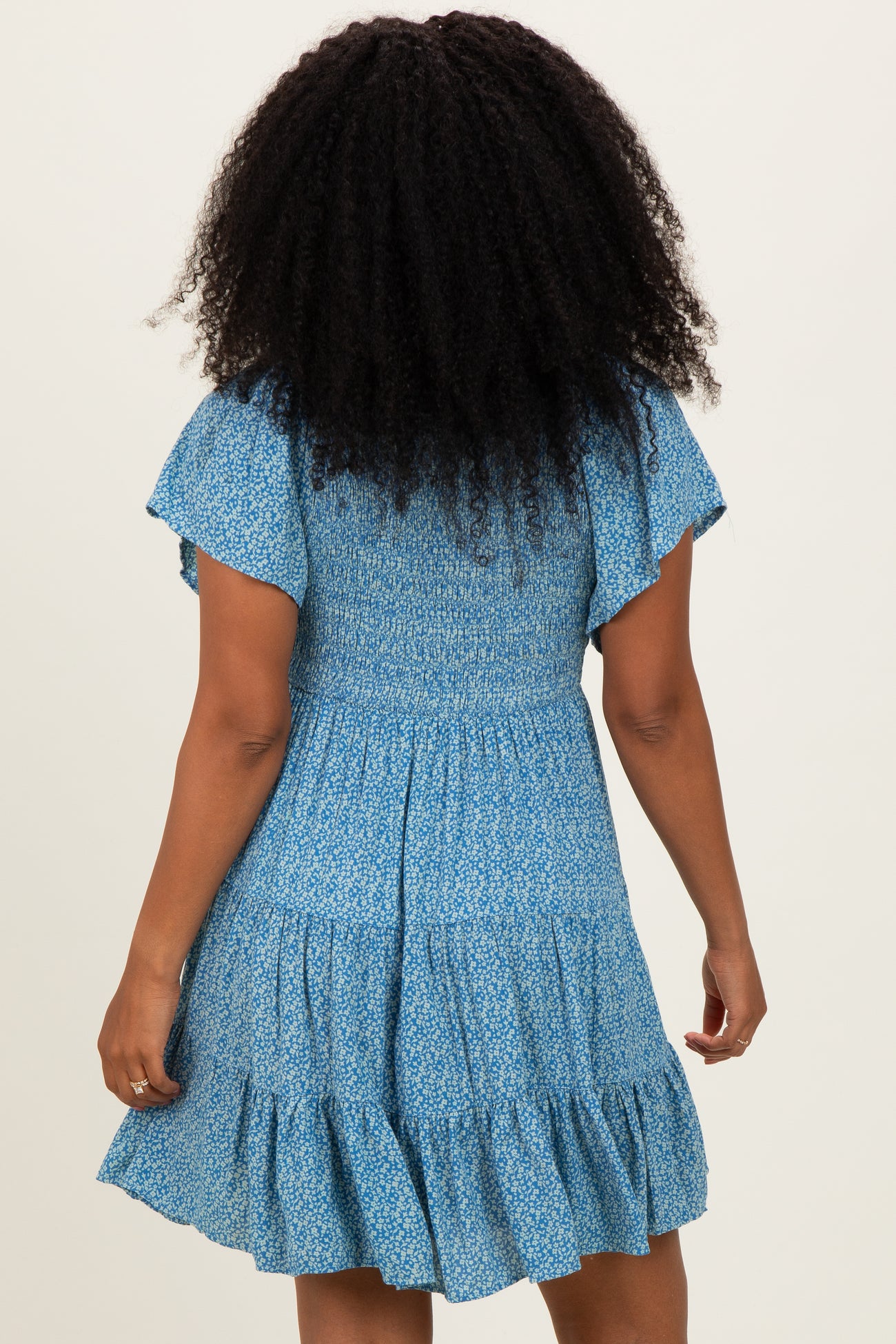 woman wearing a blue floral short sleeve dress with a smocked bodice and tiered ruffle skirt from the back