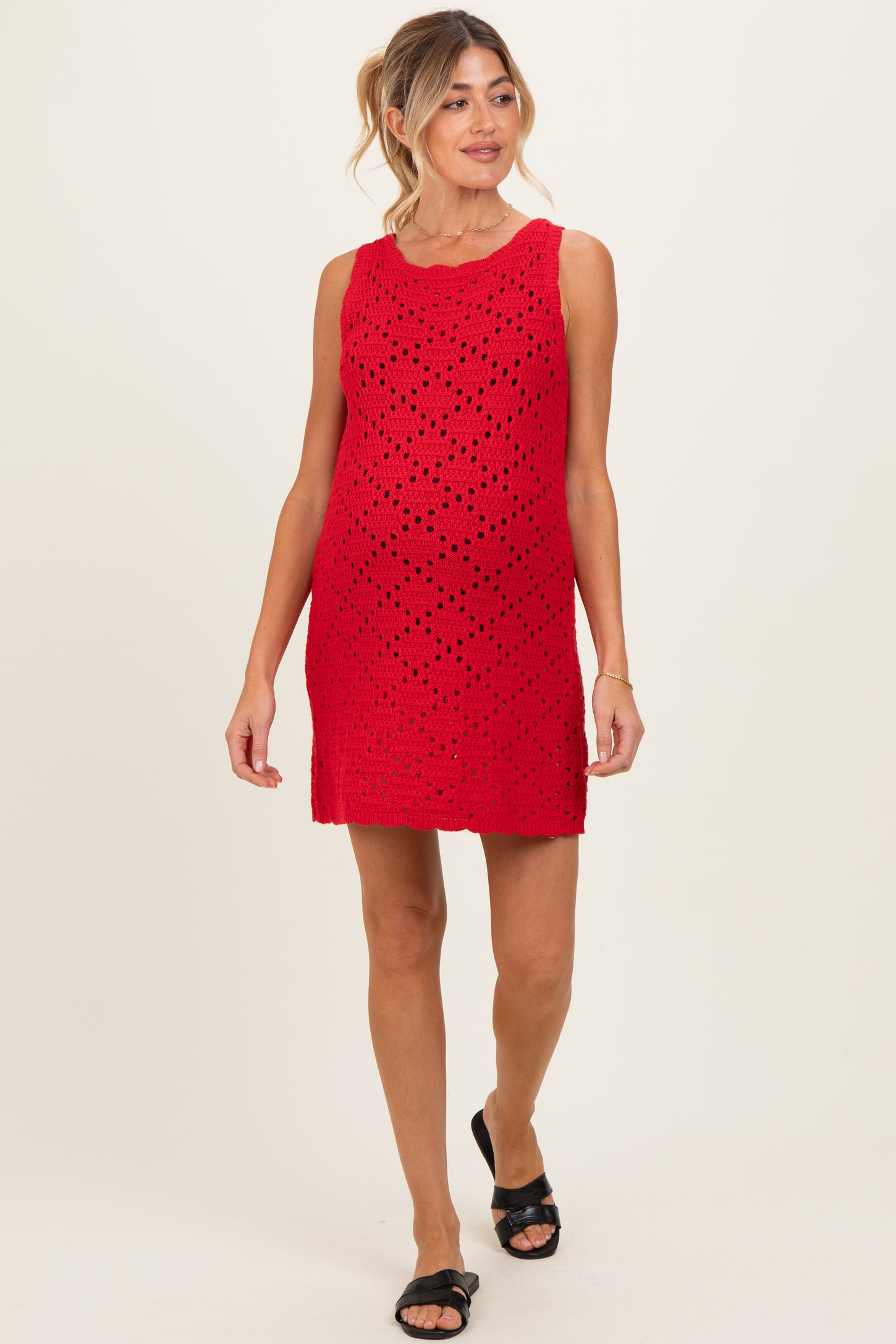 woman wearing a red sleeveless maternity dress with a perforated design and a visible baby bump