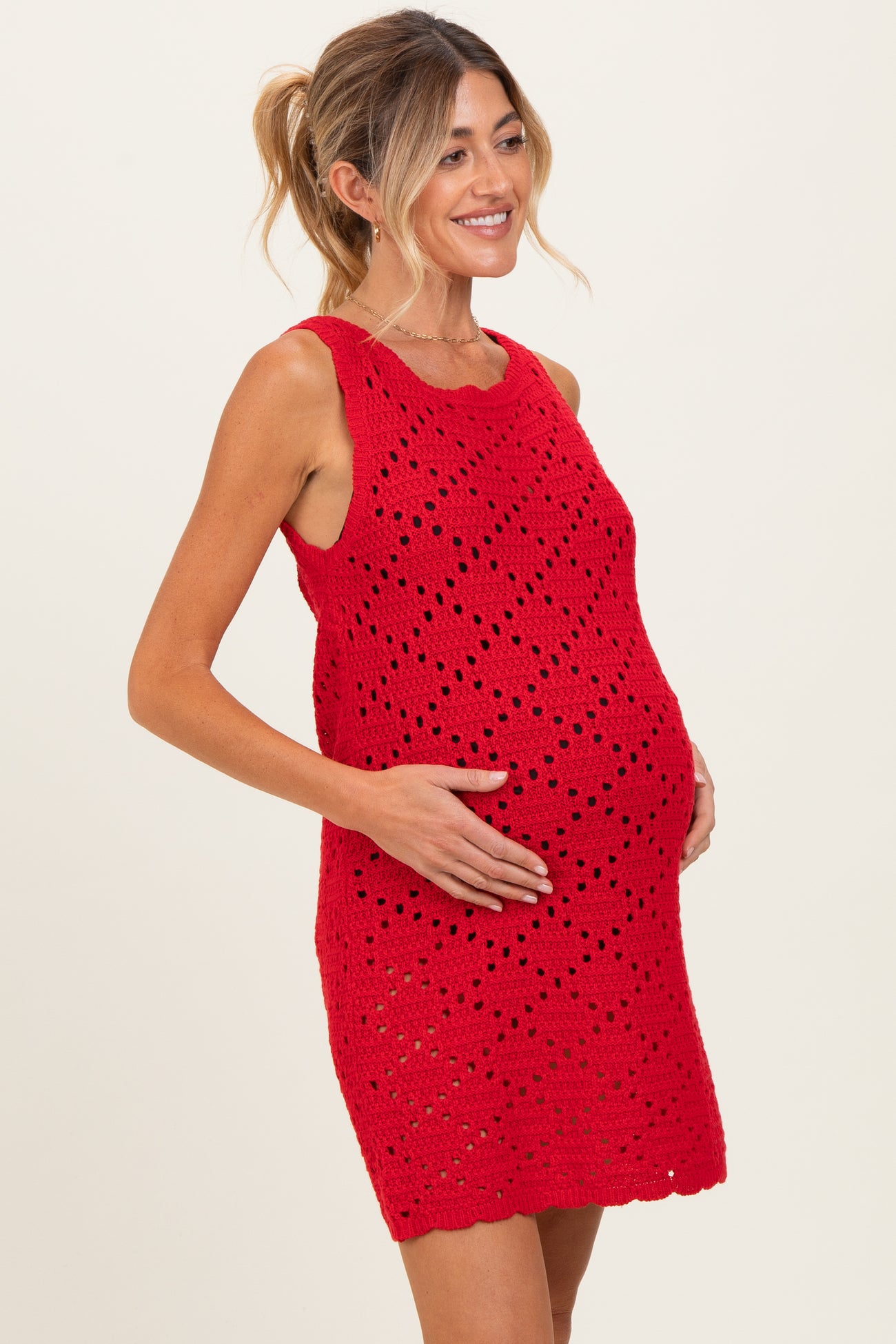 woman wearing a red crochet maternity dress and holding her baby bump