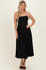 woman wearing a black spaghetti strap midi dress with a fitted bodice and flowy skirt