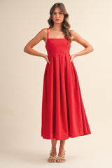 woman wearing a red spaghetti strap midi dress with a pleated skirt and posing with hands on hips