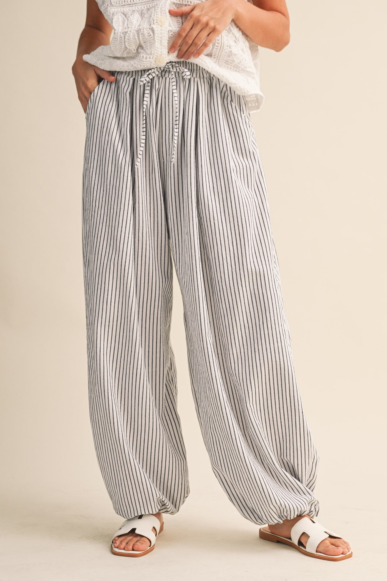 woman wearing black and white striped loose-fitting harem pants with a drawstring waist and sandals