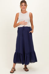 woman wearing a cream sleeveless maternity top and a dark blue tiered maxi skirt, holding her baby bump