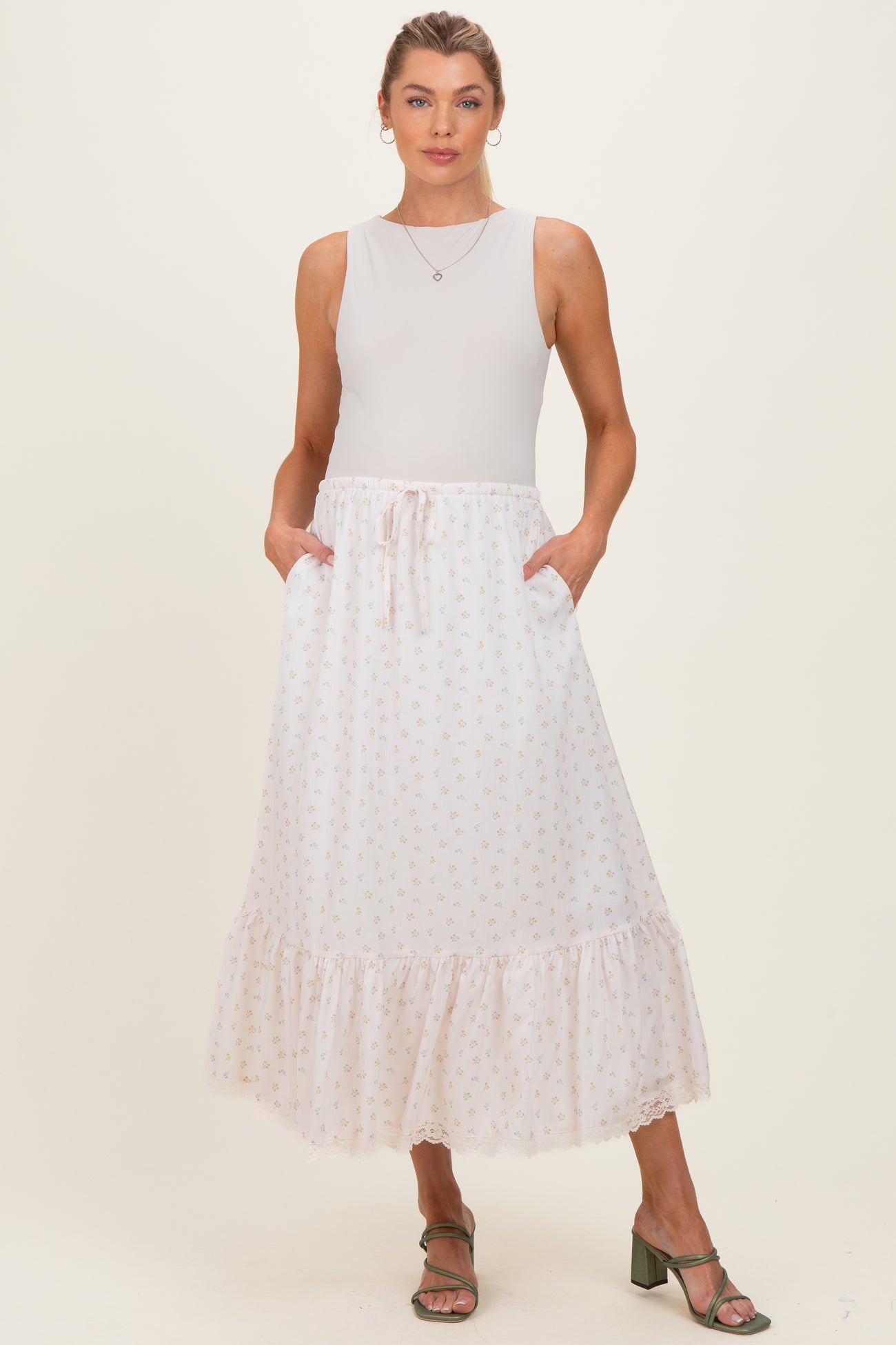 woman wearing a white floral maternity maxi skirt with pockets and a ruffled hem, paired with a sleeveless top
