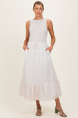 woman wearing a white floral maternity maxi skirt with pockets and a ruffled hem, paired with a sleeveless top