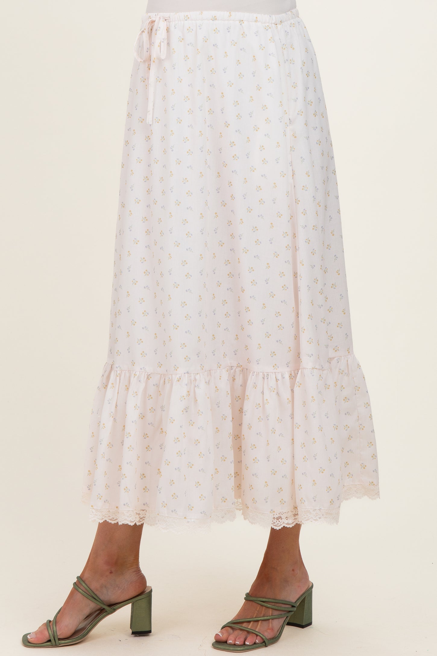 woman wearing a light pink floral maternity skirt with a ruffled hem and lace trim, standing in strappy green heels