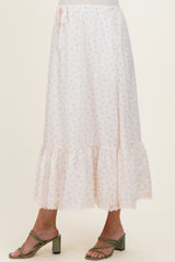 woman wearing a light pink floral maternity skirt with a ruffled hem and lace trim, standing in strappy green heels