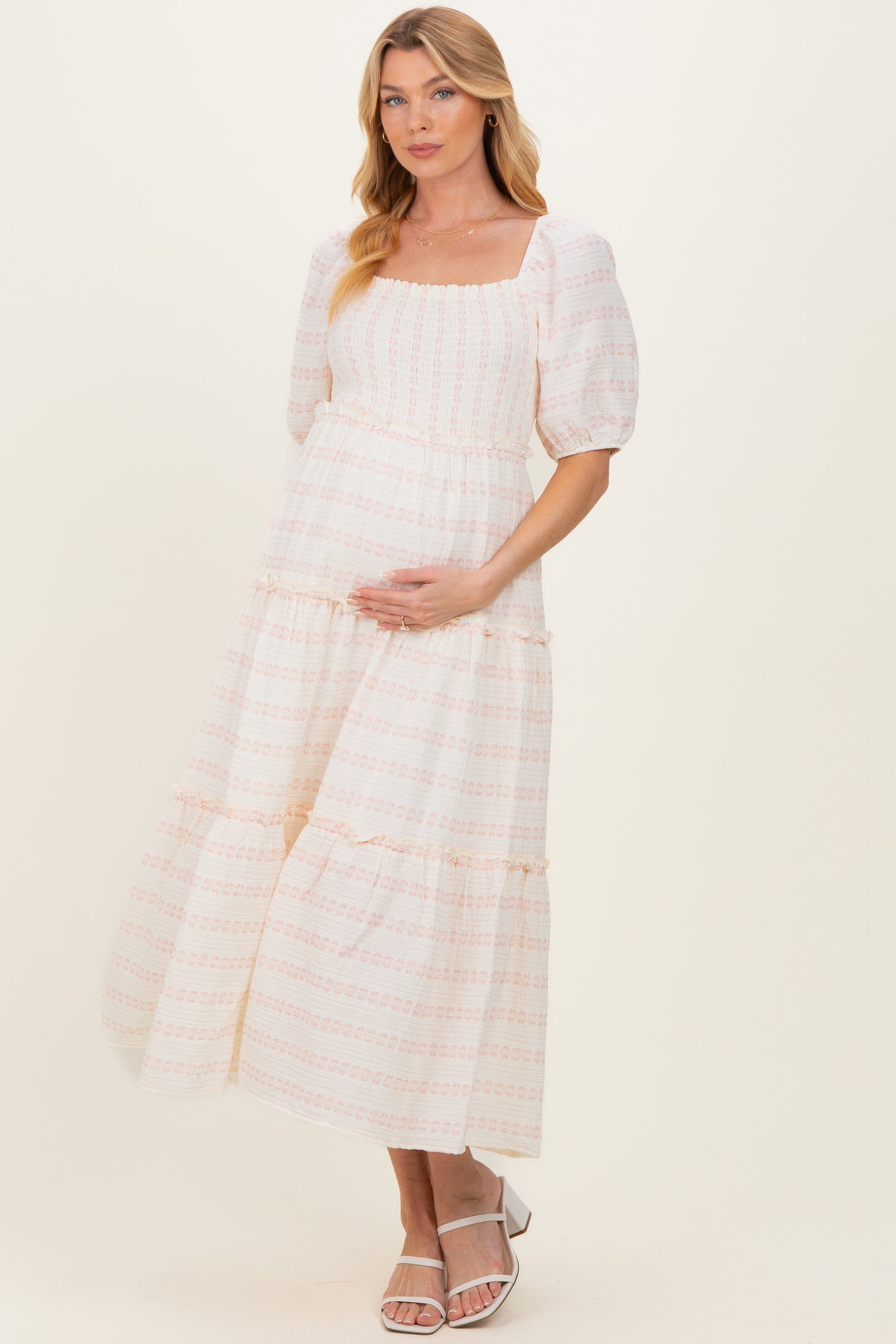 woman wearing a pink and white patterned maternity dress with puff sleeves and tiered skirt, holding her baby bump
