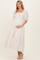 woman wearing a pink and white patterned maternity dress with puff sleeves and tiered skirt, holding her baby bump