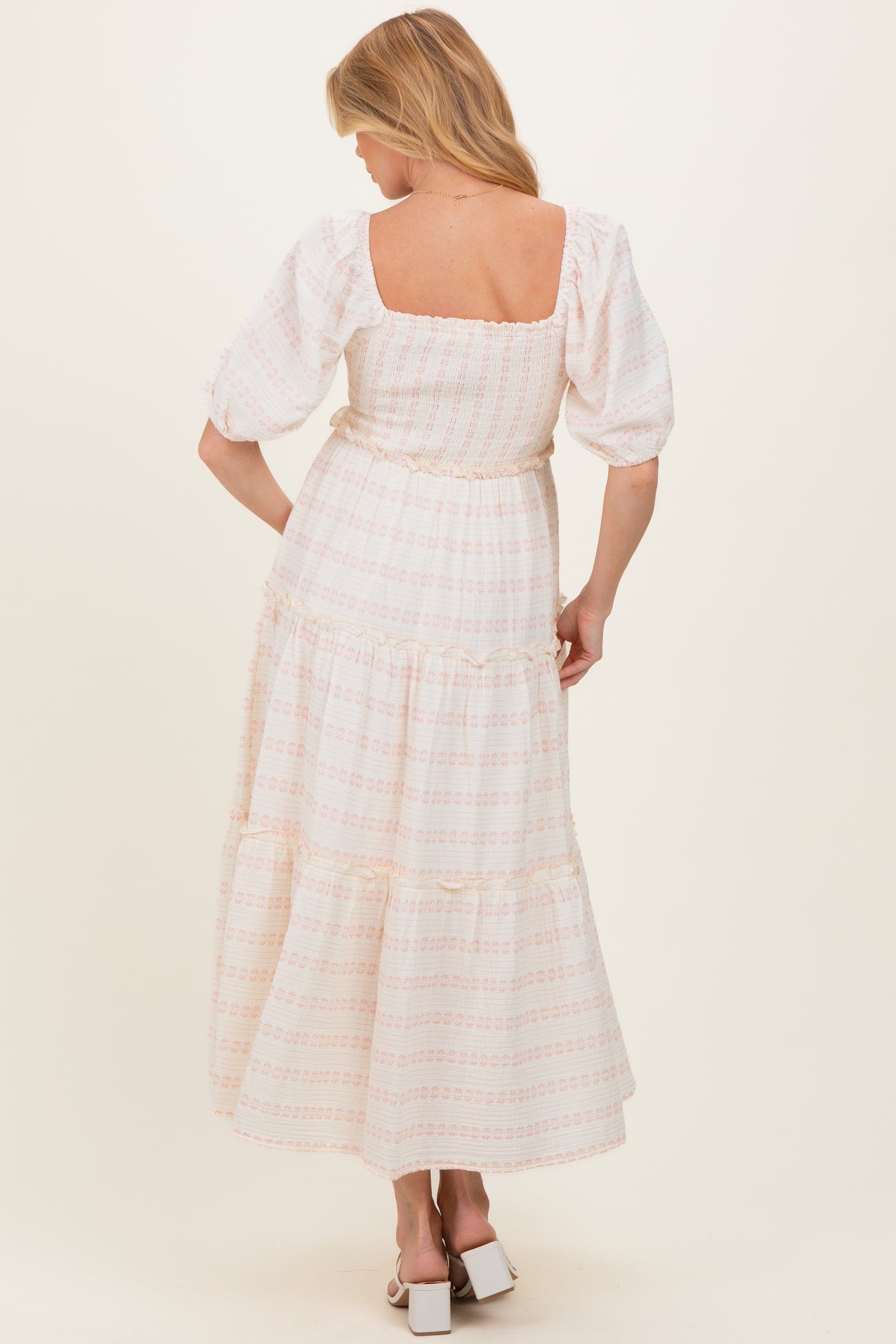 woman wearing a white maternity maxi dress with floral patterns and puff sleeves, showing her back and flowing silhouette