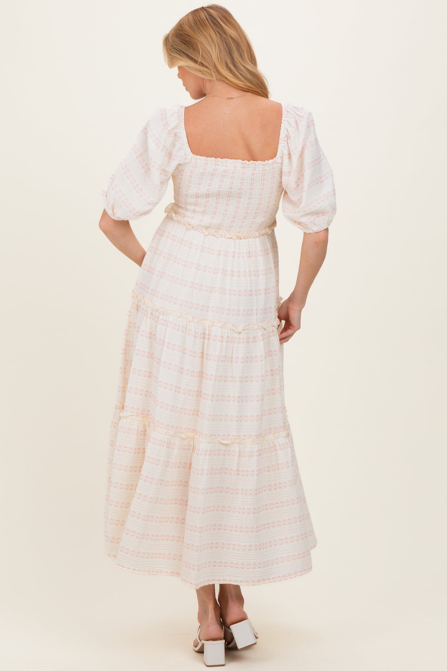 woman wearing a white maternity maxi dress with floral patterns and puff sleeves, showing her back and flowing silhouette