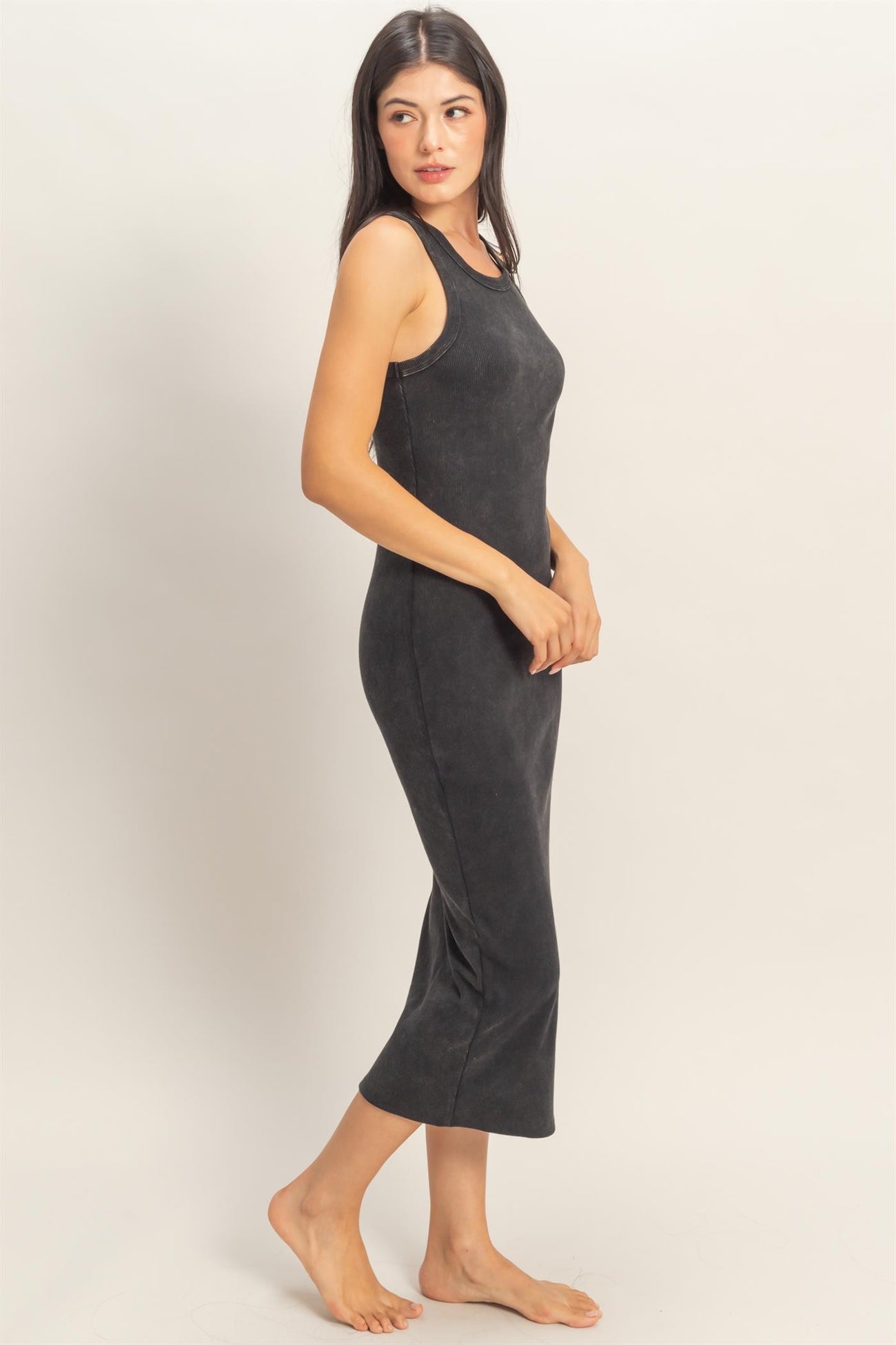 woman wearing a black ribbed midi tank dress, standing sideways with a relaxed pose