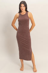 woman wearing a brown ribbed midi dress with a side slit, standing barefoot against a neutral background