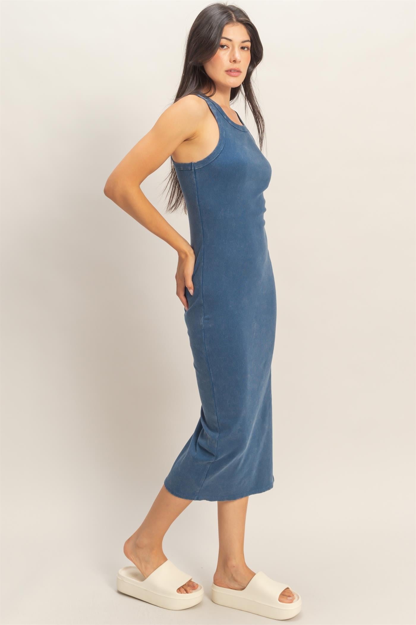 woman wearing a blue sleeveless midi dress with a fitted silhouette and side slits, paired with white platform sandals