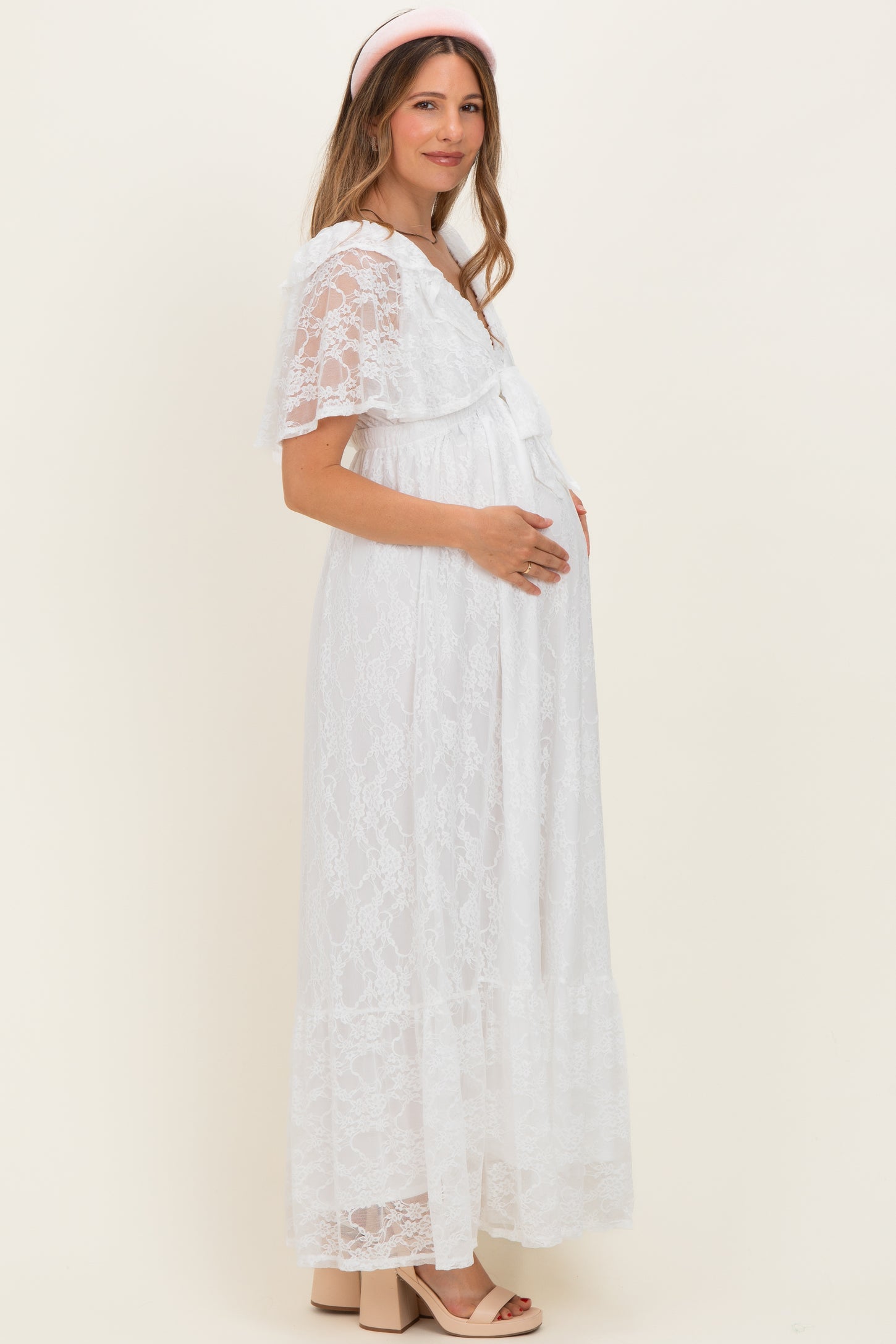 woman wearing a white lace maternity maxi dress and holding her baby bump