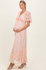 woman wearing a light pink lace maternity dress with bow detail and ruffled sleeves, showing her baby bump