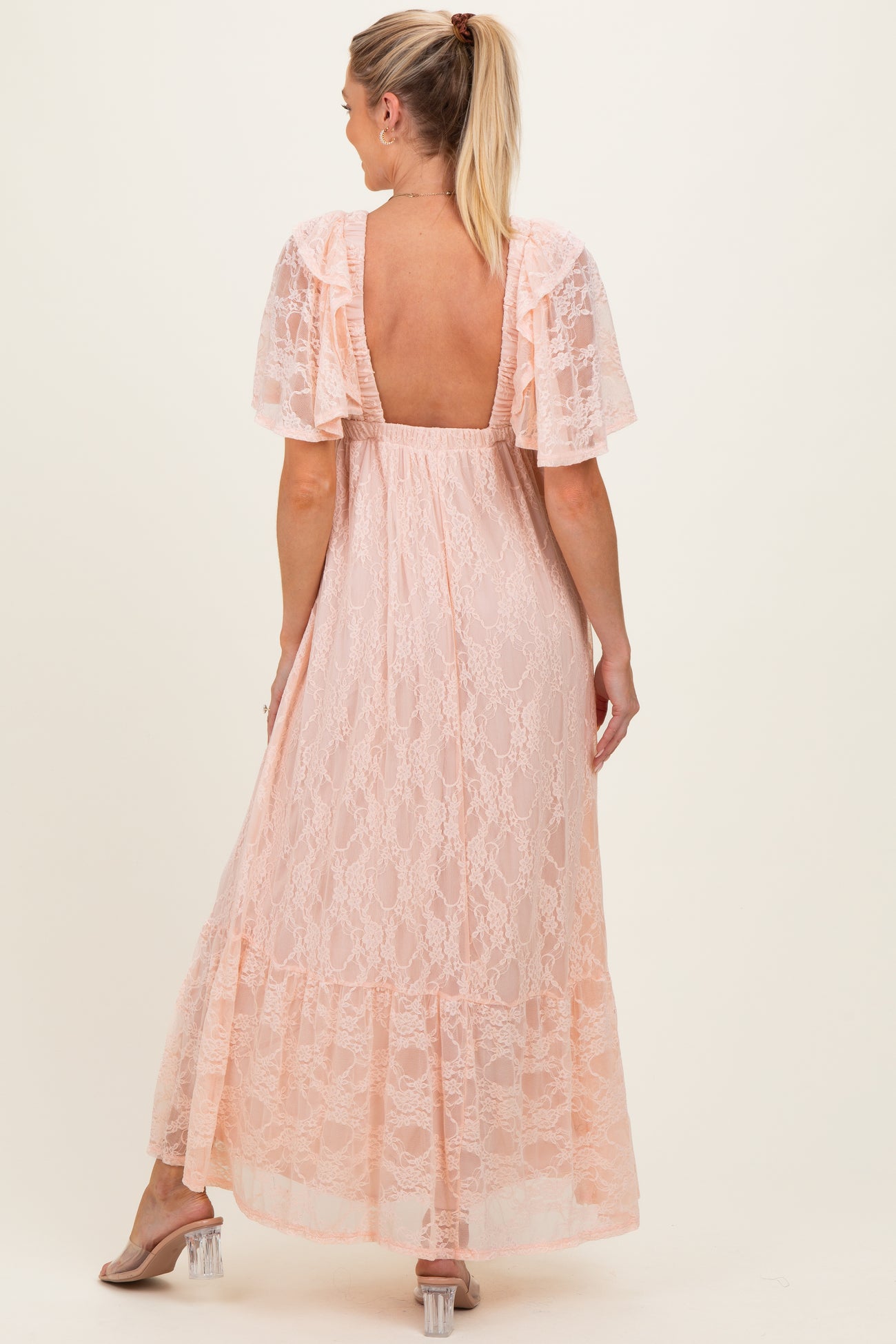 woman wearing a light pink lace maternity maxi dress with short sleeves and a backless design