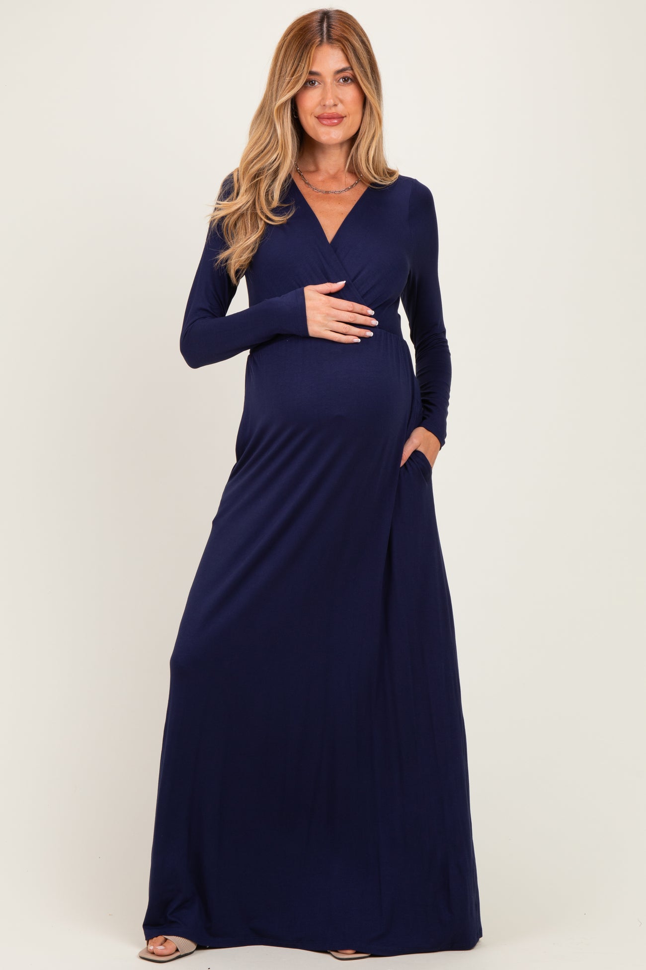 woman wearing a navy blue long sleeve maternity maxi dress and showing her baby bump with hands in pockets