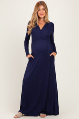 woman wearing a navy blue long sleeve maternity maxi dress with a wrap style and pockets, showing her baby bump