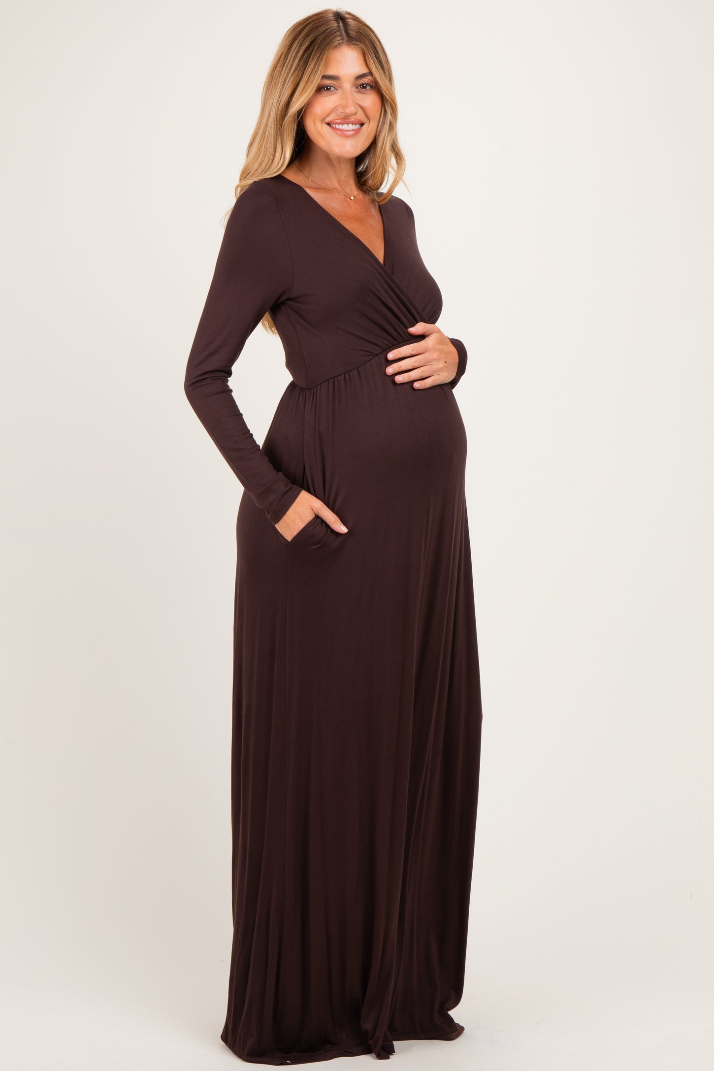 woman wearing a dark brown long sleeve maternity maxi dress with pockets and showing her baby bump
