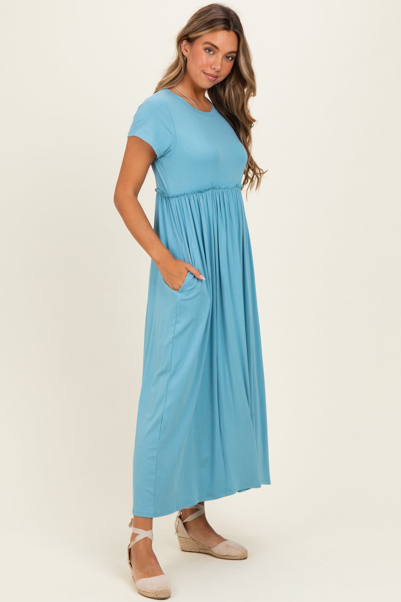 woman wearing a teal short sleeve maxi dress with a gathered waist and side pockets