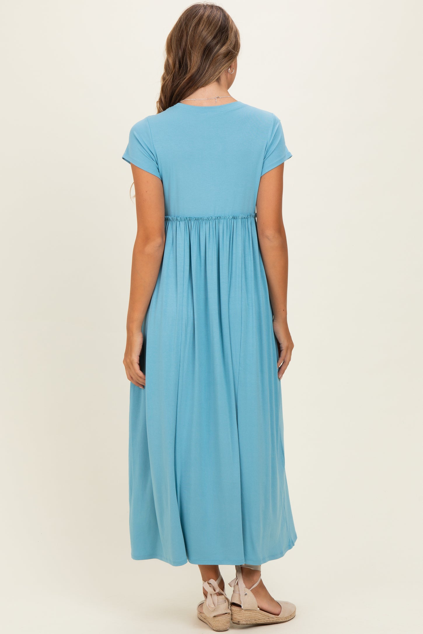 woman wearing a light blue maxi dress with cap sleeves and a gathered waist, viewed from the back