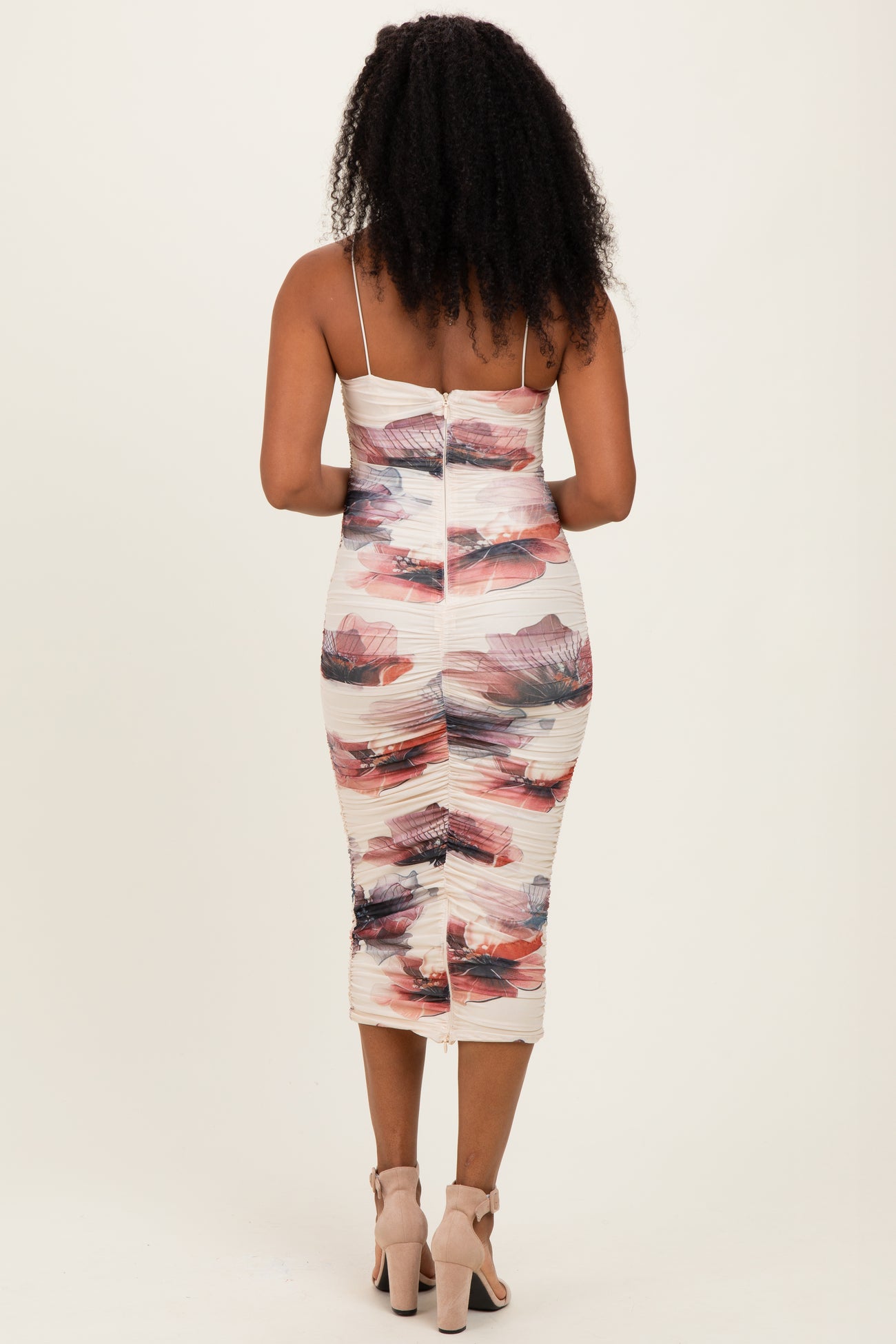 woman wearing a form-fitting midi dress with a floral print and spaghetti straps, showing the back design