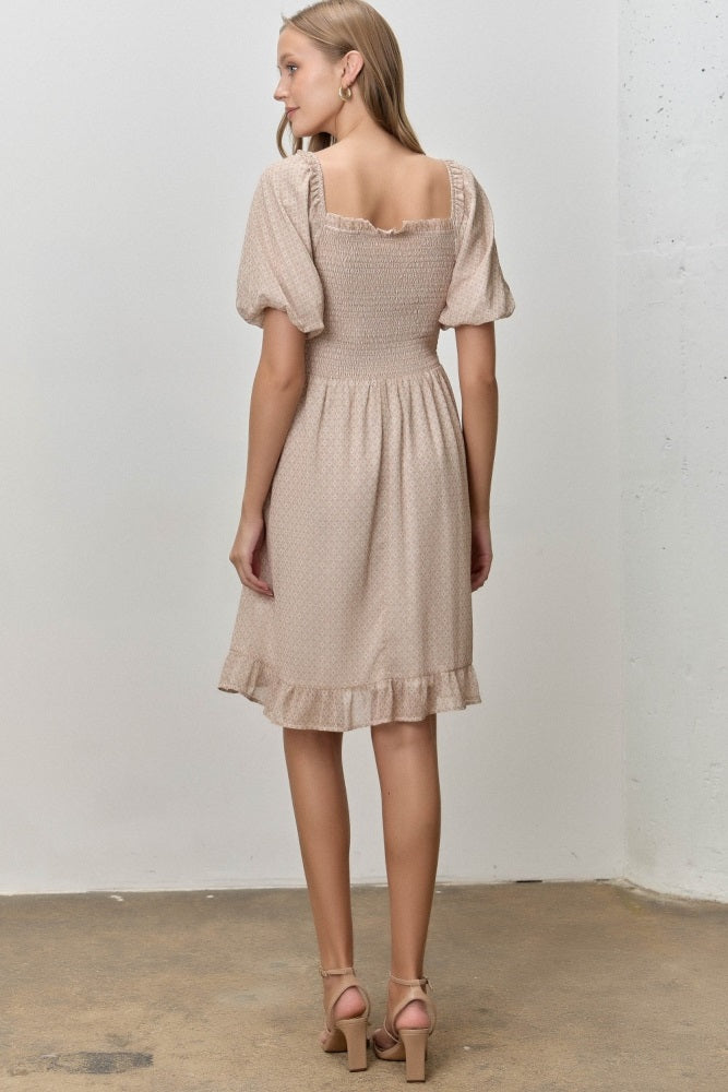 woman wearing a beige short sleeve dress with a smocked bodice and ruffled hem, viewed from the back