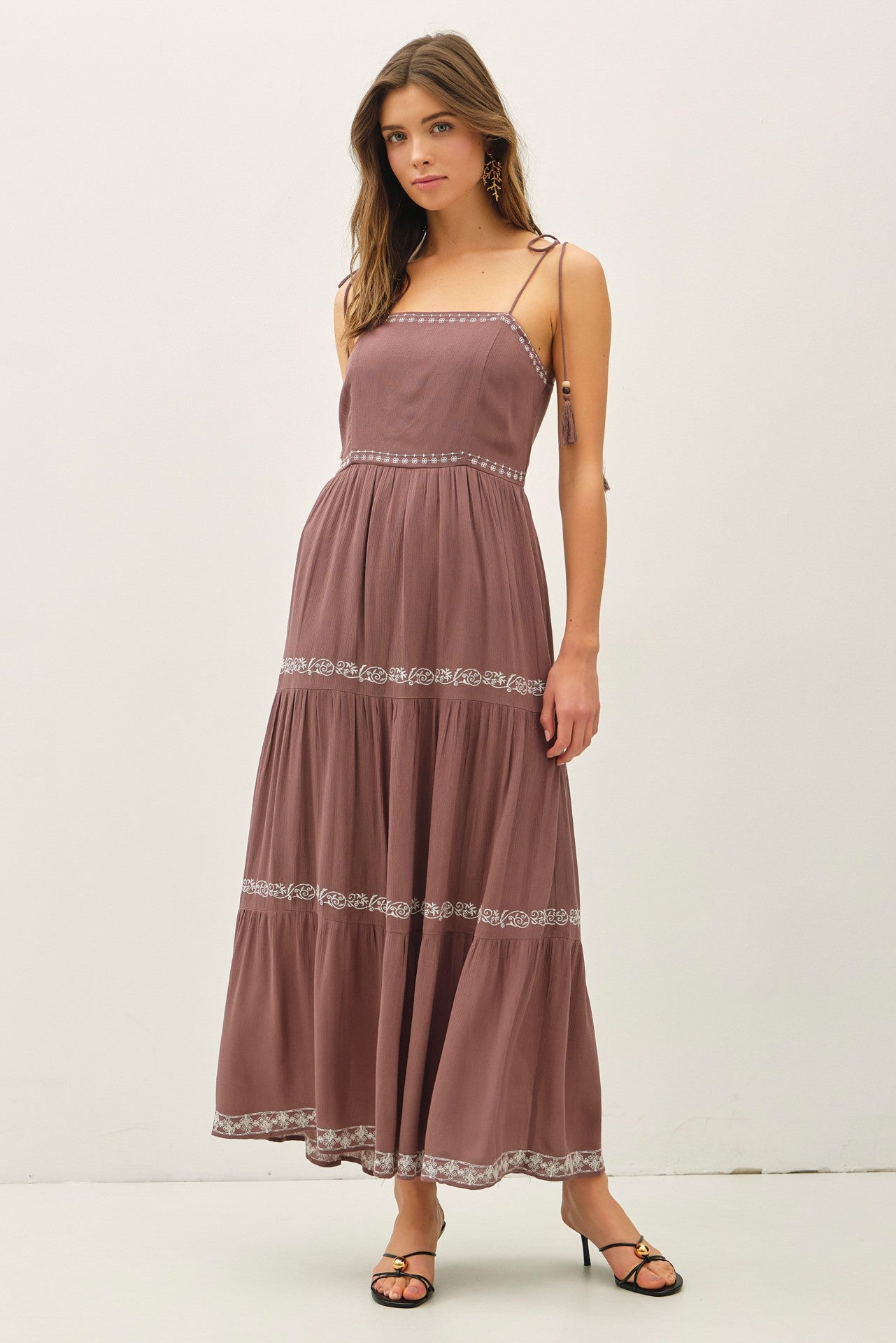 woman wearing a mauve maxi dress with spaghetti straps and floral embroidery, standing and modeling the dress