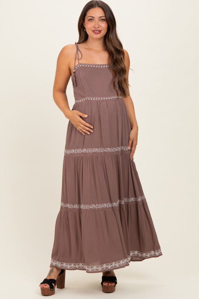 woman wearing a mauve maxi maternity dress with spaghetti straps and embroidered detailing, holding her baby bump