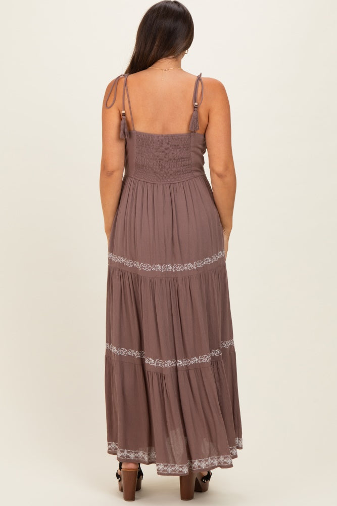 woman wearing a brown maternity maxi dress with adjustable straps and embroidered details on the tiers