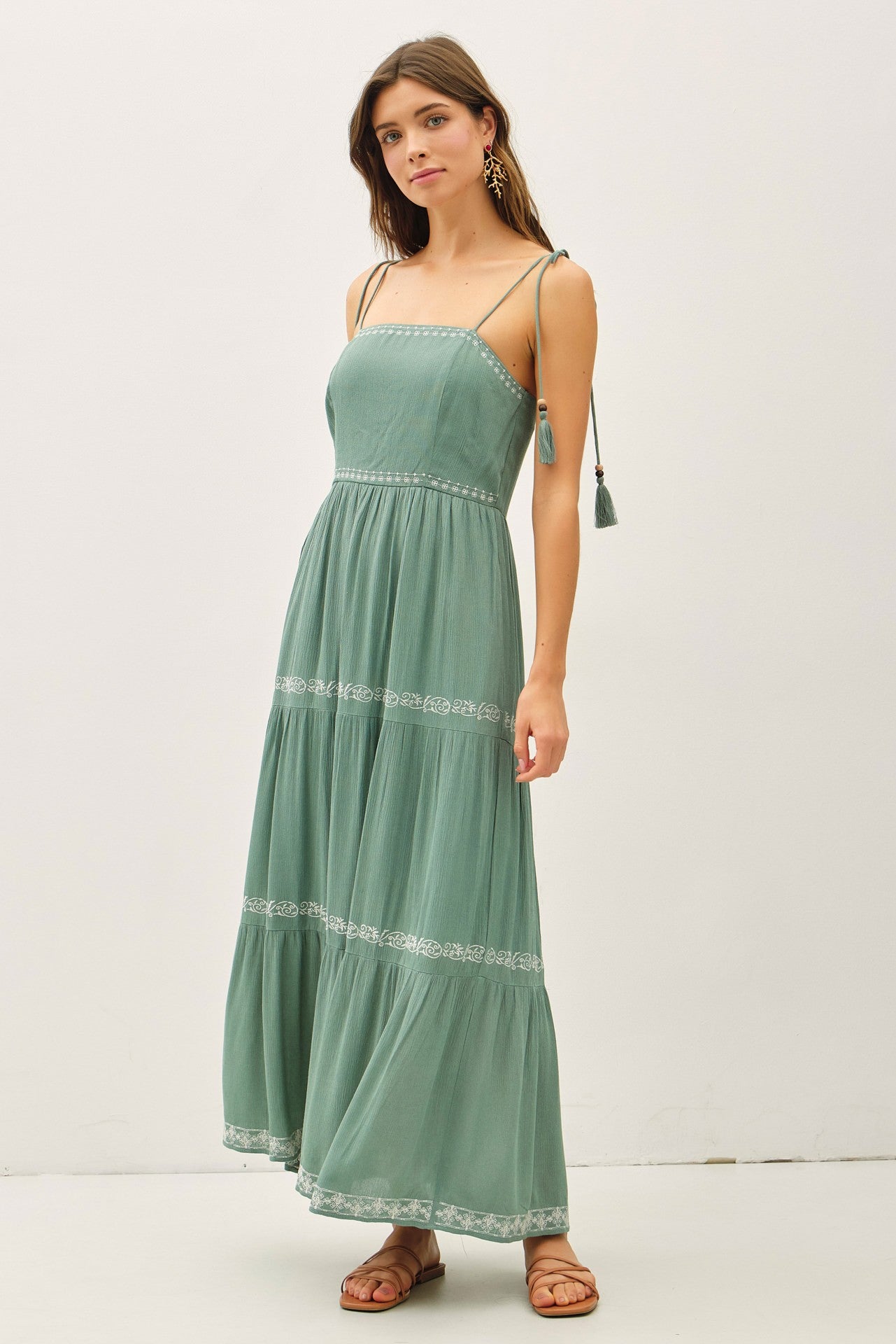woman wearing a green maxi dress with spaghetti straps and embroidered details, standing pose