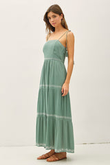 woman wearing a green maxi dress with spaghetti straps and embroidered details, standing against a plain background