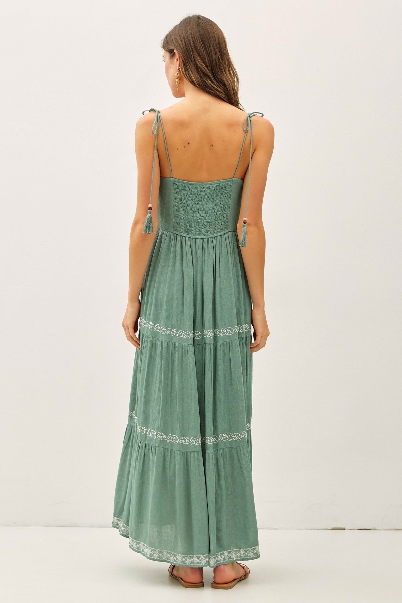 woman wearing a green maxi dress with adjustable straps and embroidered details, shown from the back