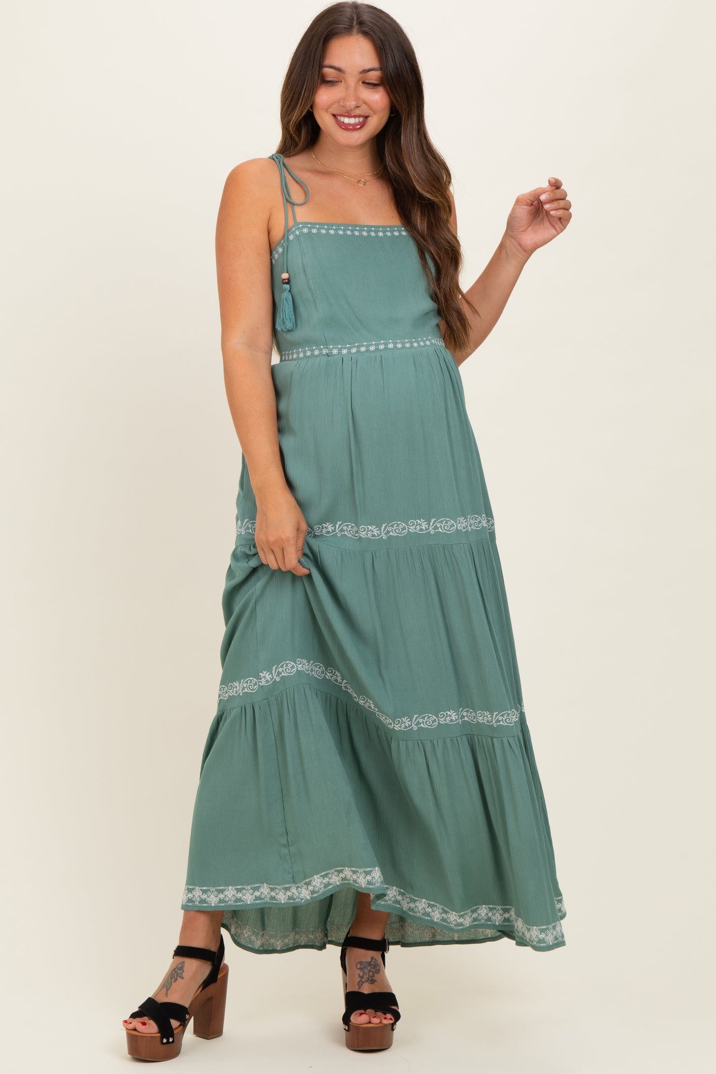 woman wearing a green maternity maxi dress with lace detailing and adjustable straps, showcasing her baby bump