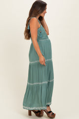 woman wearing a green maternity maxi dress with embroidery details and a visible baby bump