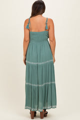 woman wearing a teal long maxi maternity dress with smocked bodice and trim details, showing a baby bump from the back