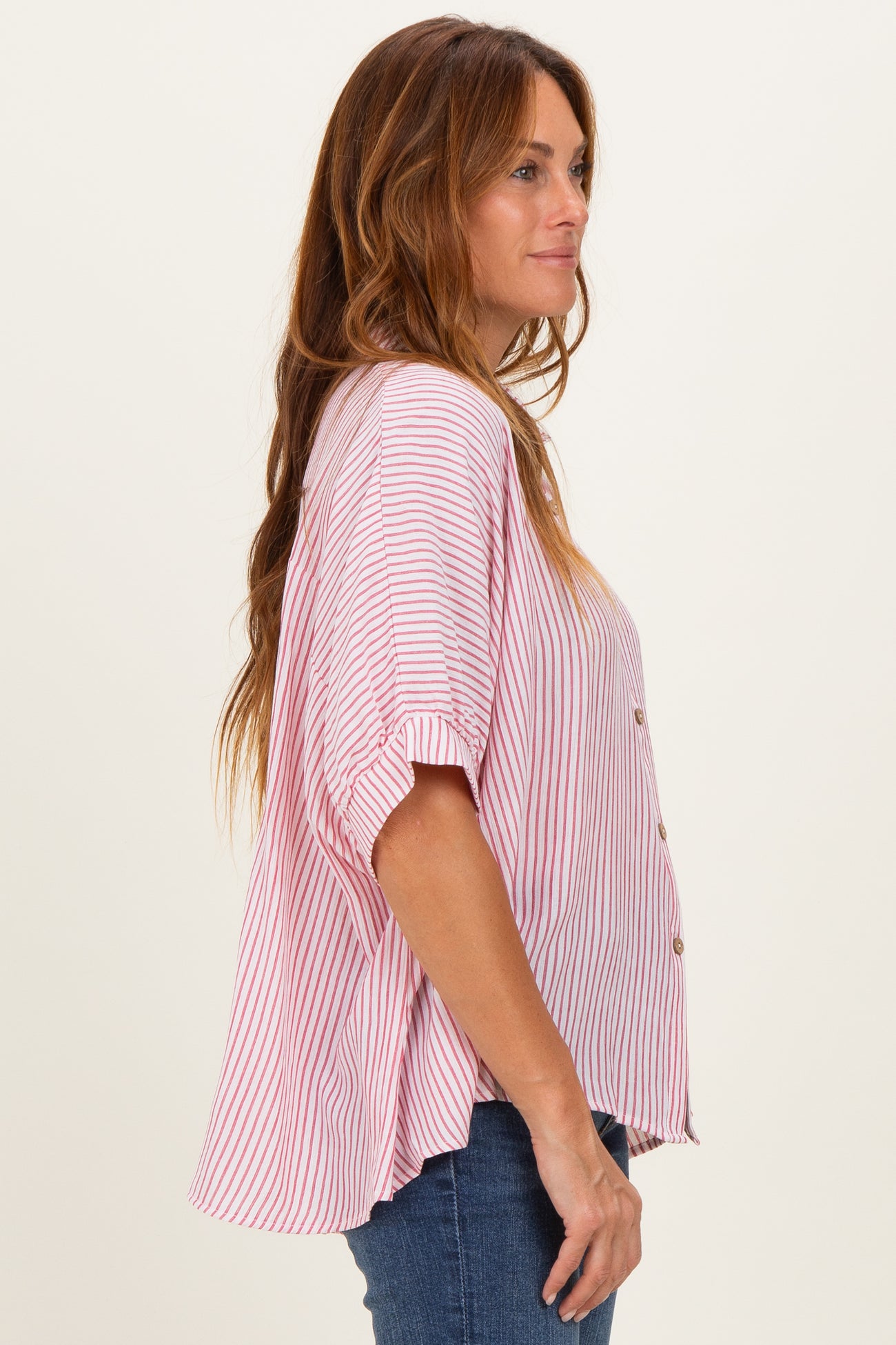 woman wearing a pink and white striped button-up top with rolled sleeves and a relaxed fit, paired with denim jeans