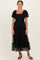 woman wearing a black tiered puff sleeve maxi dress with a smocked bodice and sheer overlay, standing in black heels