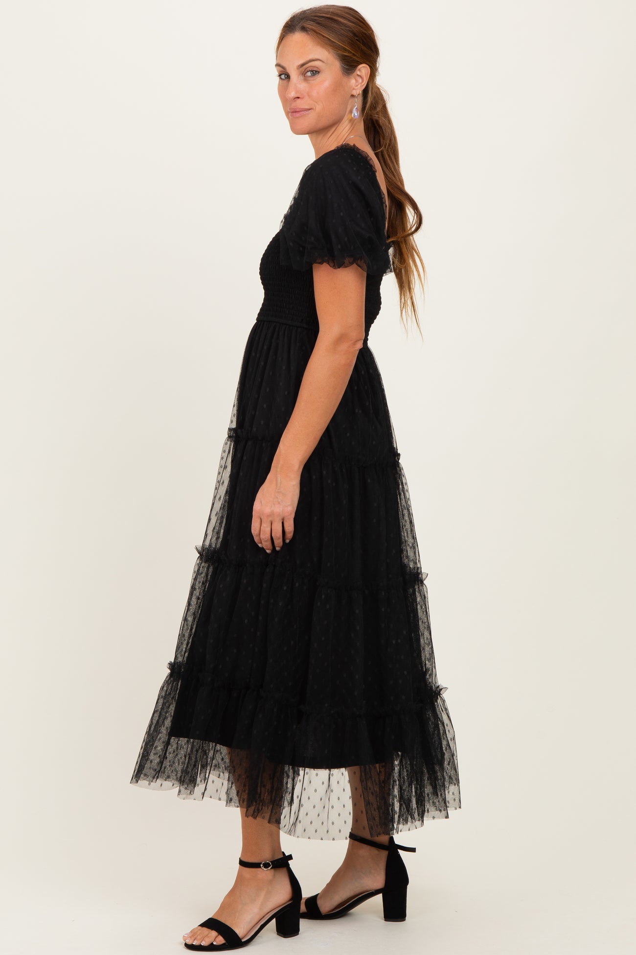 woman wearing a black tiered tulle midi dress with puff sleeves and a fitted bodice, standing in profile