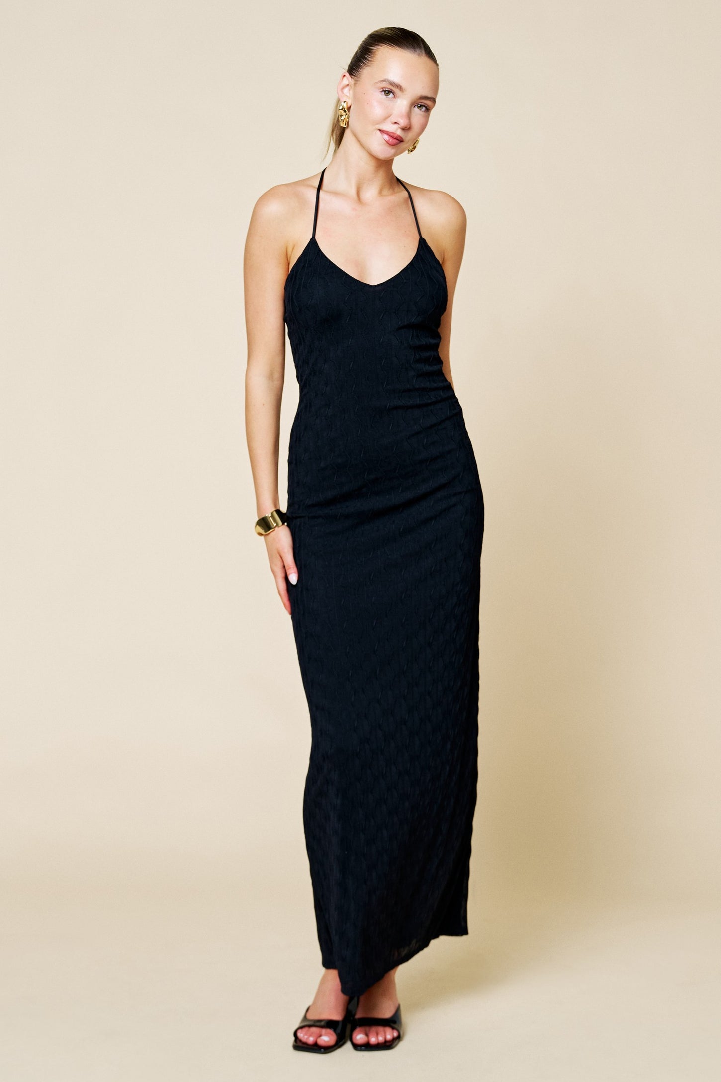 woman wearing a black halter neck maxi dress with a fitted silhouette and textured fabric
