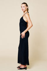 woman wearing a black halter neck maxi dress with a textured pattern and strappy back, standing against a beige background